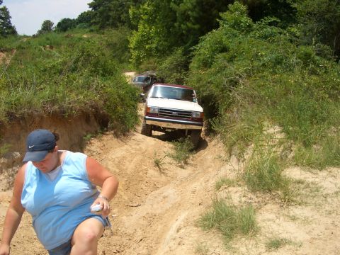 1990 Ford Bronco - A white and maroon Ford Bronco navigates a sandy off-road trail with another vehicle behind it.