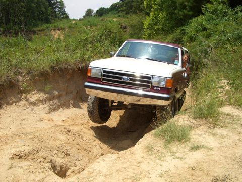 1990 Ford Bronco - Ford Bronco navigates a challenging off-road obstacle on a dirt trail.