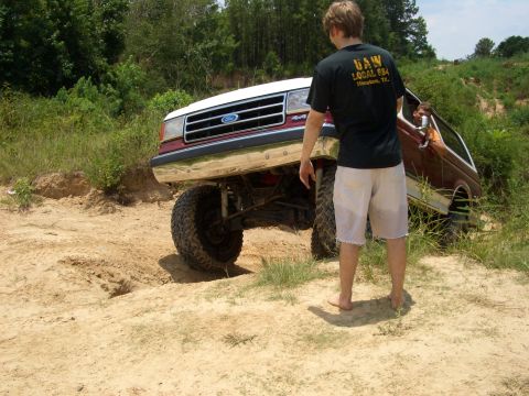 1990 Ford Bronco - A lifted Ford Bronco navigates a sandy, off-road course with a person observing.