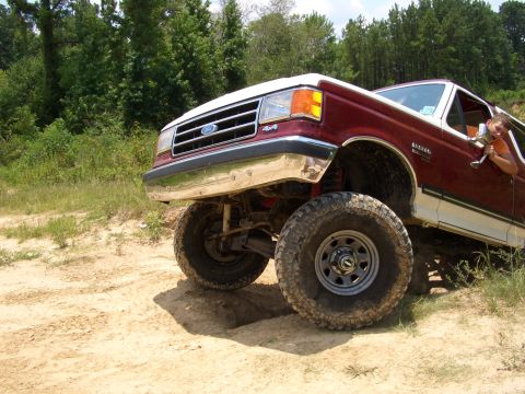 1990 Ford Bronco - A maroon and white Ford Bronco with a lifted suspension is shown off-road.