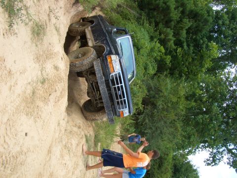 1990 Ford Bronco - A 1990 Ford Bronco is stuck in a sandy ditch while onlookers observe the situation.