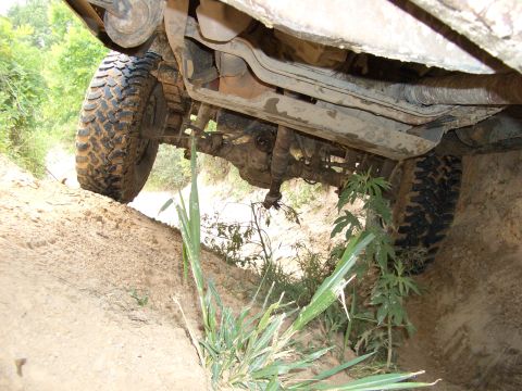 1990 Ford Bronco - The underside of a vehicle navigates a rough, off-road terrain with visible suspension components and tires.