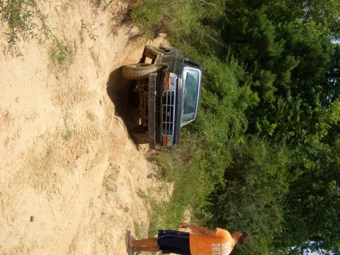 1990 Ford Bronco - A black 1990 Ford Bronco navigates a steep dirt incline surrounded by lush green trees.