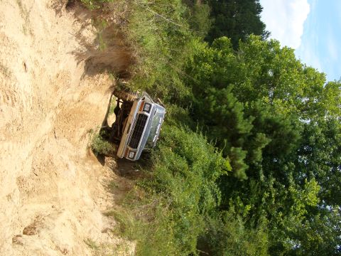 1990 Ford Bronco - A silver SUV navigates a steep, sandy incline surrounded by dense green trees.