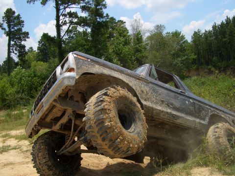 1990 Ford Bronco - This heavily modified Ford Bronco is shown off-road, kicking up dirt as it ascends a hill.