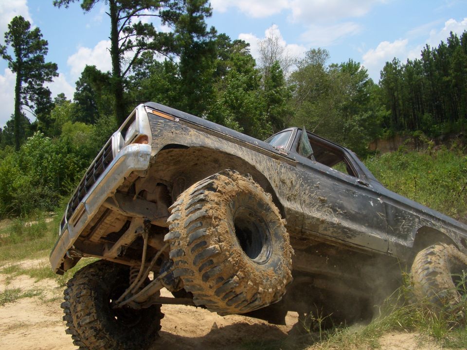 Mud-covered dark gray Ford Bronco with large off-road tires climbing a dirt incline