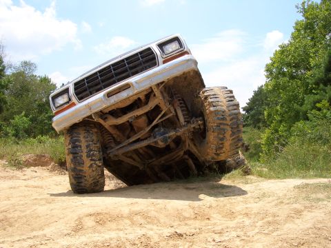 1990 Ford Bronco - Ford Bronco tilted on its side during off-road activity, revealing its undercarriage and large tires.