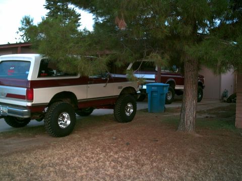 1988 Ford Bronco - A lifted Ford Bronco and a pickup truck are parked outside a building.