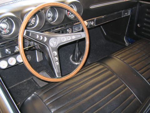 1969 Ford Ranchero - The interior of a classic car features a wood-rimmed steering wheel and pleated black vinyl seats.