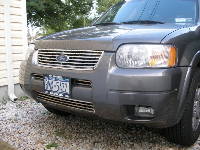 Front end close-up of gray Ford Escape with chrome grille, Ford oval and New York plate