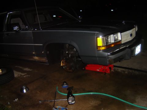 1988 Ford Crown Victoria LTD - A dark gray 1988 Ford Crown Victoria LTD is shown with its front wheel removed and supported by a jack.