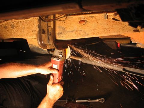 1995 Ford Bronco - Mechanic uses an angle grinder on a vehicle's rusty underbody, creating a shower of sparks.