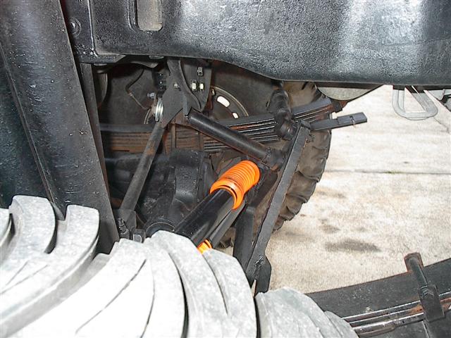 Truck rear suspension with leaf springs and orange shock absorber. Close-up view