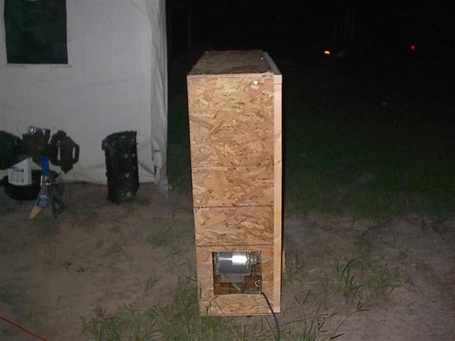 wooden box with a motor inside, next to a white tent and some engine parts