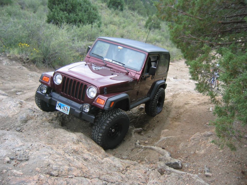 Maroon Jeep Wrangler on rocky terrain, front-left tire angled up