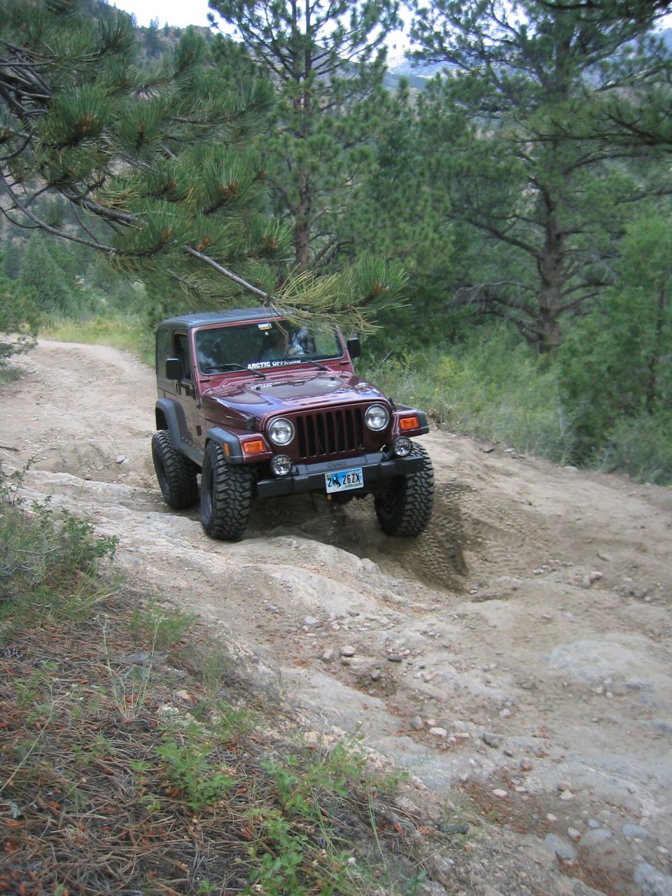 Maroon 1997 Jeep Cherokee on a dirt trail, front-left tire angled up a rock