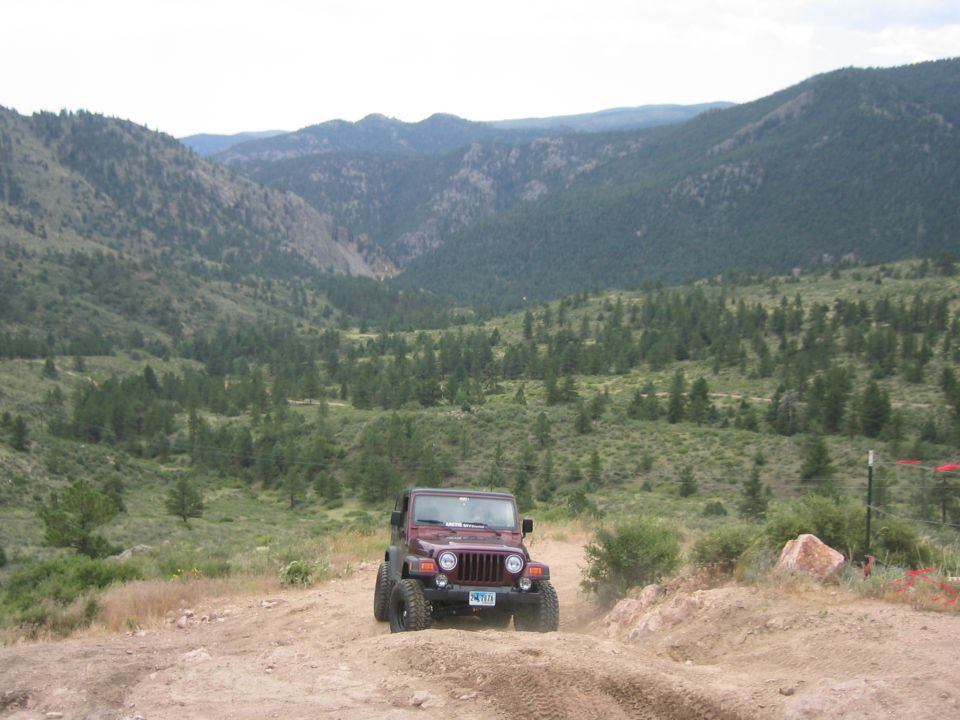Maroon Jeep Wrangler on a dirt road with mountains in the background