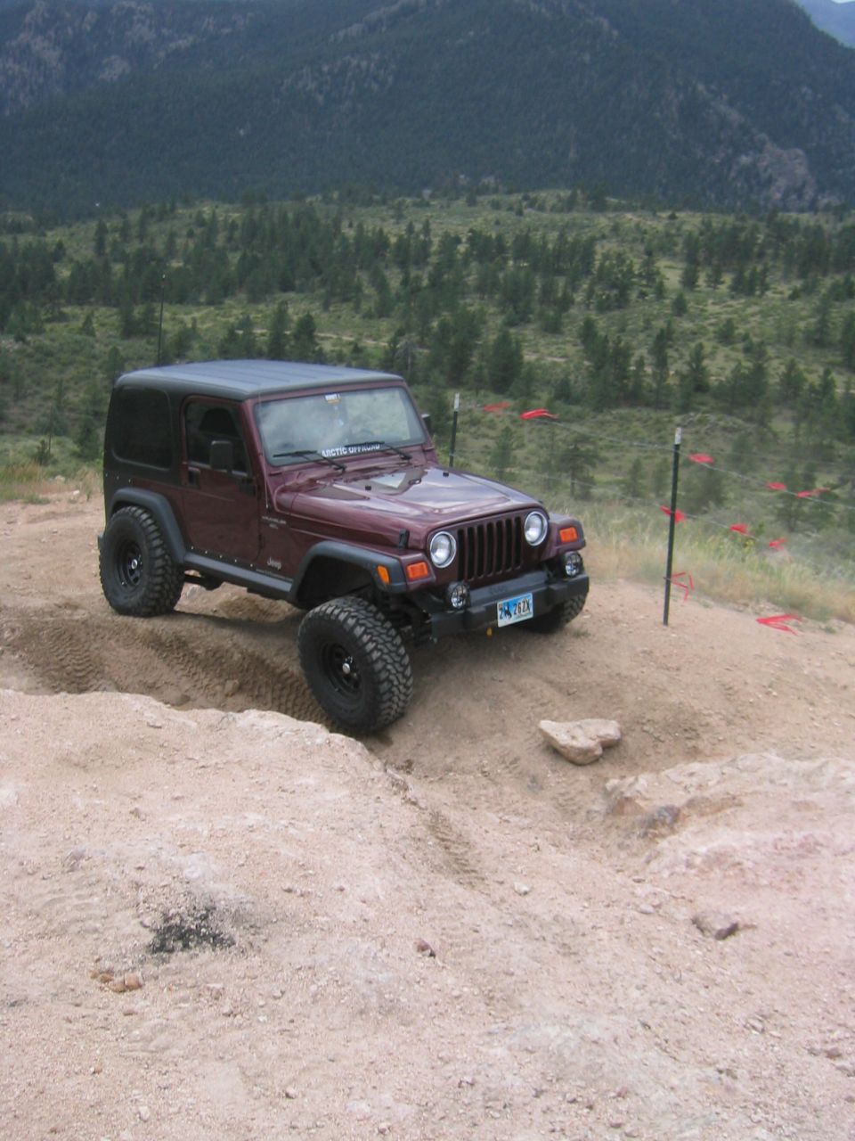 Maroon Jeep Wrangler TJ on dirt trail, front 3/4 view. License plate visible