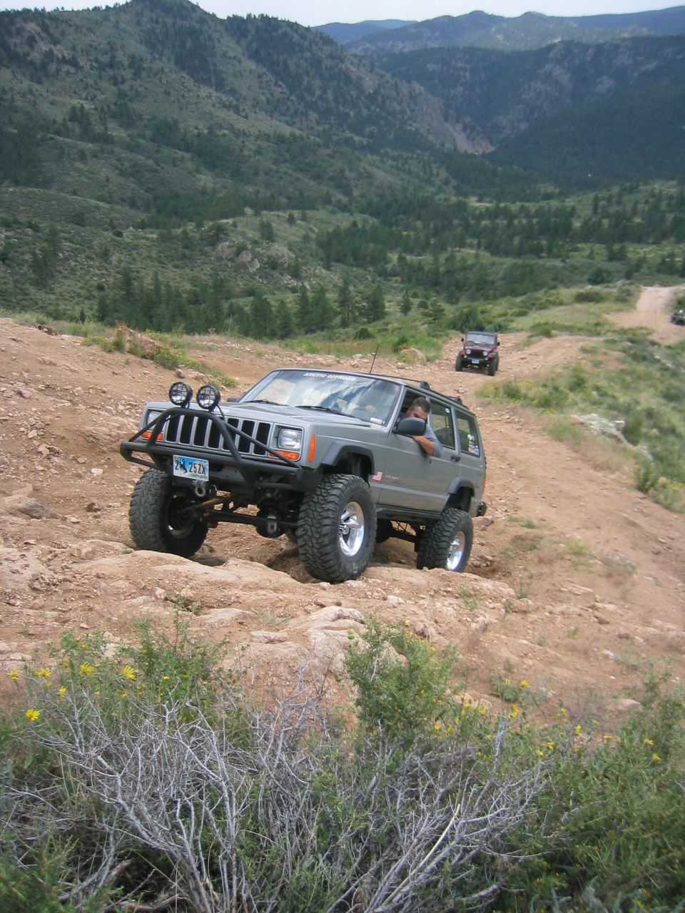 Gray Jeep Cherokee on a dirt trail with a driver. Other vehicles are visible further up the path