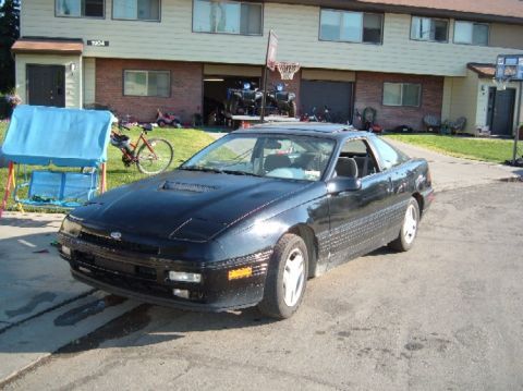 1989 Ford Probe - A black 1989 Ford Probe is parked in front of a residential building with a basketball hoop visible.