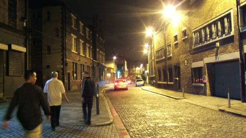 1988 Mercury Sable - A nighttime street scene in England shows people walking and cars driving down a cobblestone road lined with brick buildings.