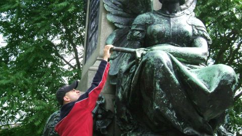1988 Mercury Sable - A man in a red jacket and black cap interacts with a large, verdigris-covered bronze statue in an outdoor setting.