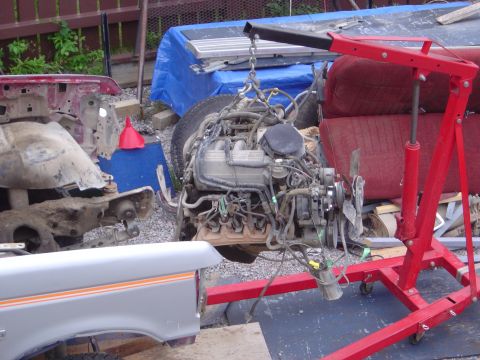 1986 Ford F-150 - Engine and vehicle parts are visible in this outdoor scene, with a red engine crane and a disassembled truck.