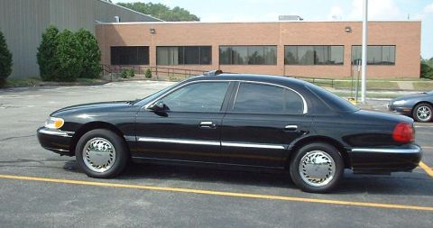 1997 Ford Crown Victoria - A black sedan is parked in a lot with a brick building behind it.