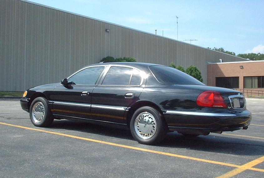 Black sedan parked in a lot, rear three-quarter view. Chrome trim and hubcaps visible
