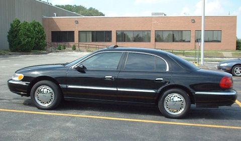 1997 Ford Crown Victoria - Side view of a black Lincoln Town Car parked in a lot next to a brick building.