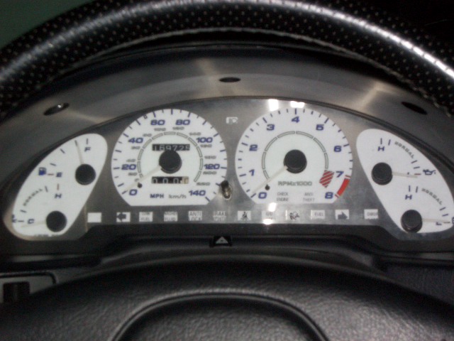White-face gauge cluster with blue numbers seen through steering wheel, odometer at 189725 miles