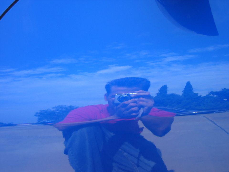 Glossy blue car paint reflecting photographer with camera, showing mirror-finish polish