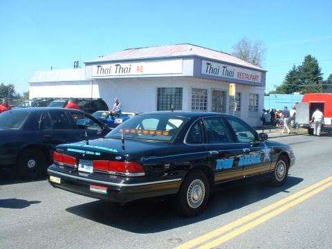 1999 Ford Crown Victoria - A black sedan, possibly a 1999 Ford Crown Victoria, is parked on a street in front of a Thai restaurant.