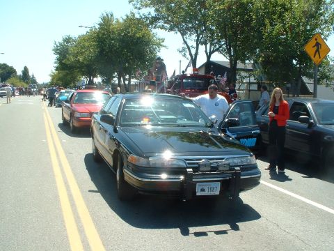 1999 Ford Crown Victoria - A black 1999 Ford Crown Victoria police car is parked on the street, possibly during a parade or event.