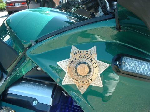 1999 Ford Crown Victoria - A King County Sheriff's motorcycle is shown with its official badge and a light bar. Another vehicle is parked behind it.