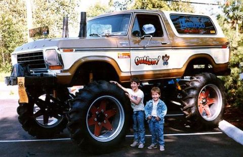 1979 Ford Bronco - A modified 1978 Ford Bronco with oversized tires and custom decals stands next to two children.