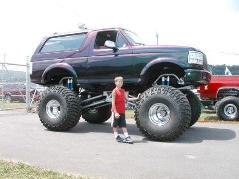1979 Ford Bronco - A boy stands next to a heavily modified monster truck with large tires and a custom paint job.