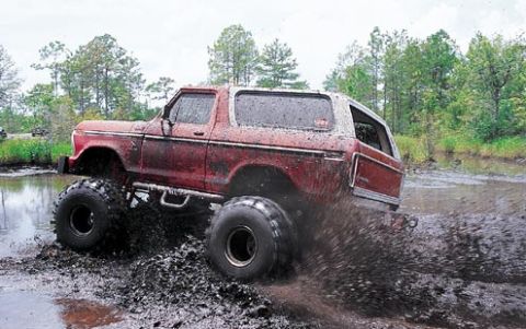 1979 Ford Bronco - This lifted SUV is navigating a muddy terrain, kicking up a significant amount of mud as it moves.