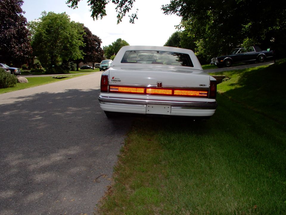 White Lincoln Town Car sedan viewed from the rear with full-width taillight, parked on a lawn