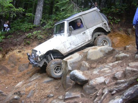 1991 Ford Bronco - A white Jeep Wrangler tackles a challenging off-road course with steep inclines and large rocks.