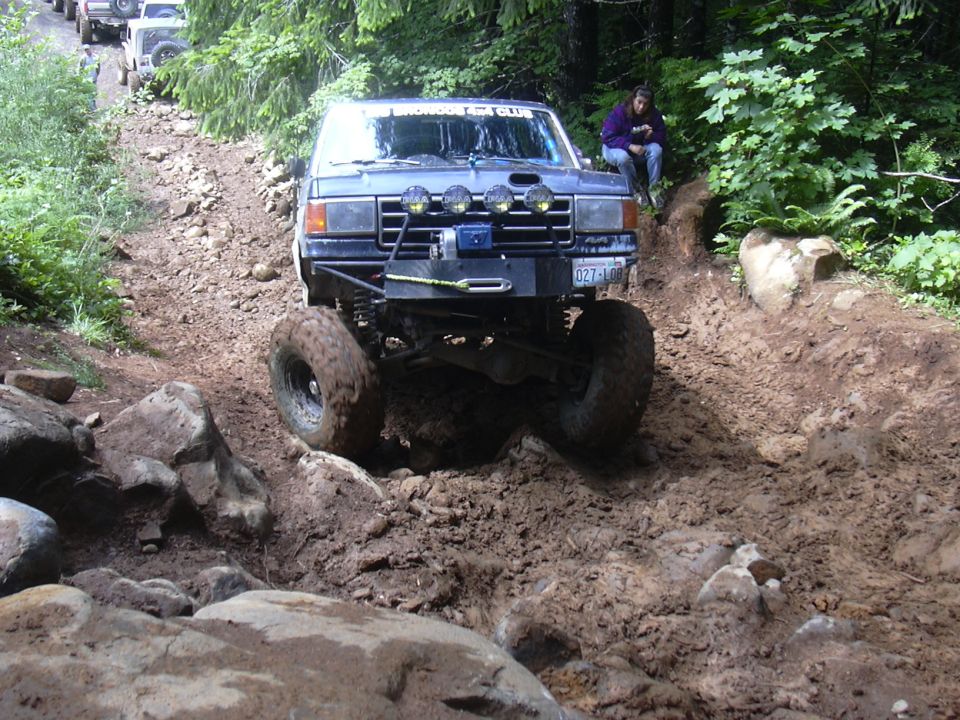 Blue off-road SUV with large tires climbing a muddy, rocky incline. License plate reads 027-LBO