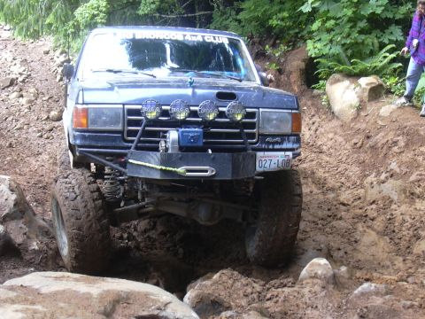 1991 Ford Bronco - Off-road SUV with winch and auxiliary lights navigates a challenging muddy trail.