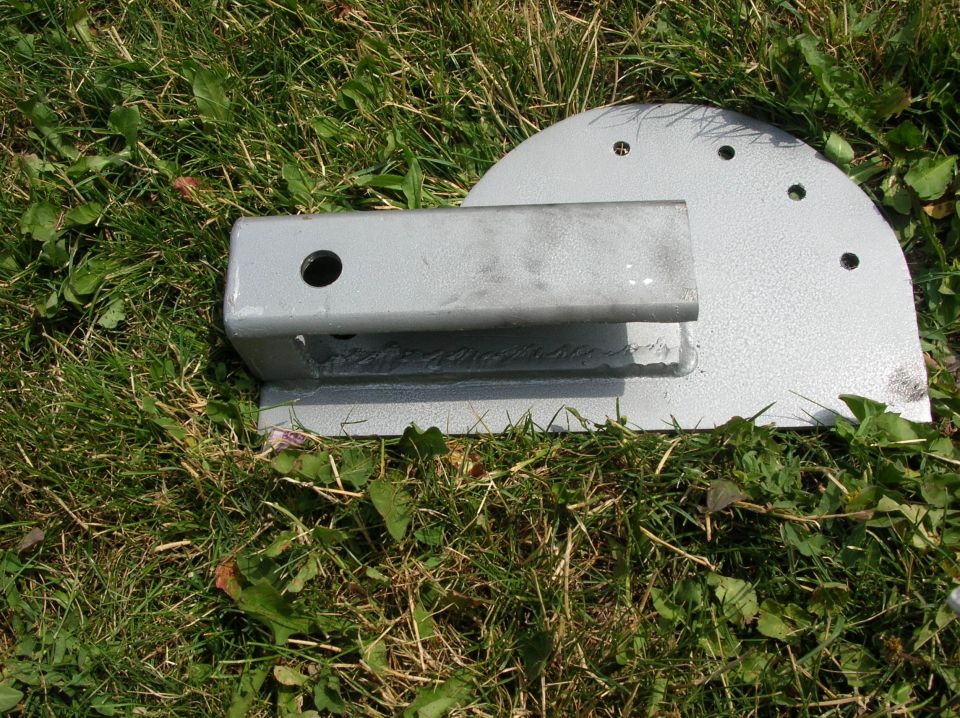 Gray welded receiver tube on a semicircular drilled steel plate, laying in grass