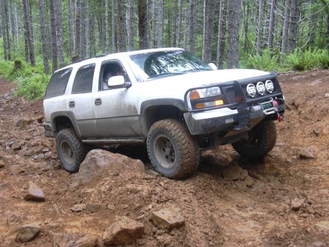 1991 Ford Bronco - White Chevrolet Tahoe navigating a challenging off-road course through a forest.