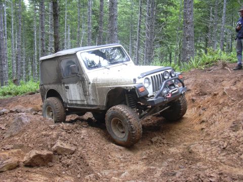 1991 Ford Bronco - A white Jeep Wrangler navigates a challenging muddy off-road course.