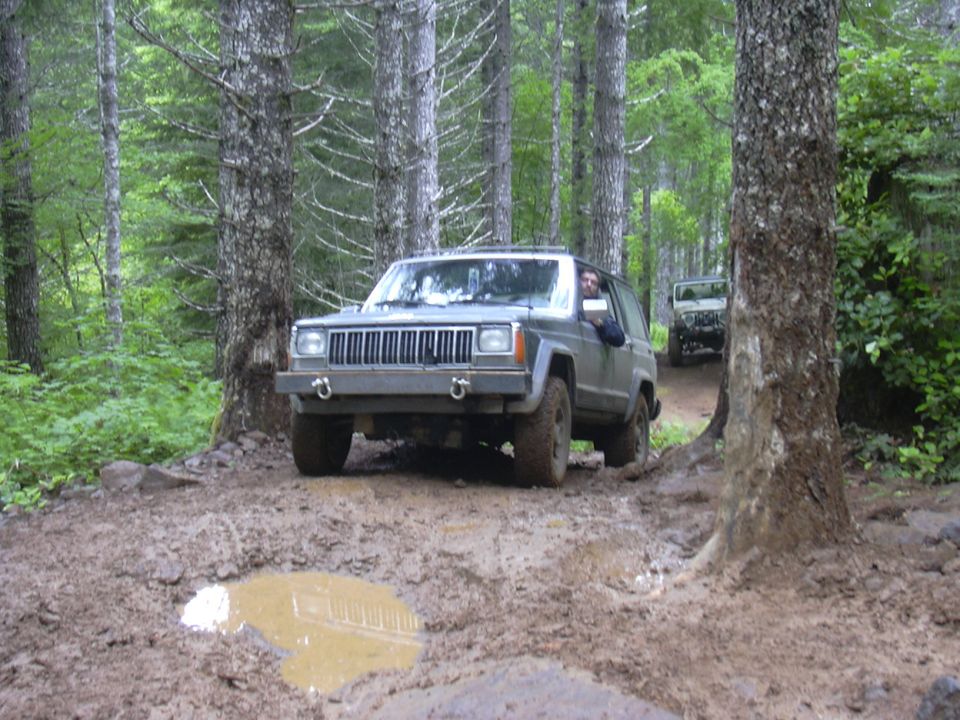 Gray Jeep Cherokee XJ driving through mud on a forest trail, another Jeep follows