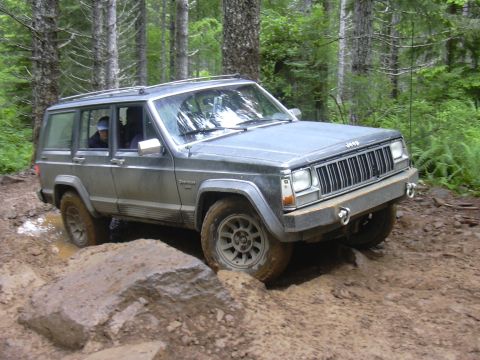 1991 Ford Bronco - Jeep Cherokee XJ tackles a challenging muddy obstacle on a forest trail.