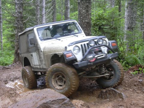 1991 Ford Bronco - A white Jeep Wrangler TJ tackles a challenging muddy off-road course.