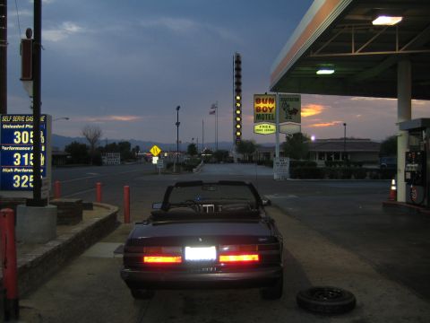 1985 Ford Mustang - Convertible at a gas station in the evening, with a motel sign and sunset visible.