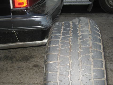 1985 Ford Mustang - Worn tire tread is visible next to the rear bumper of a dark-colored vehicle.